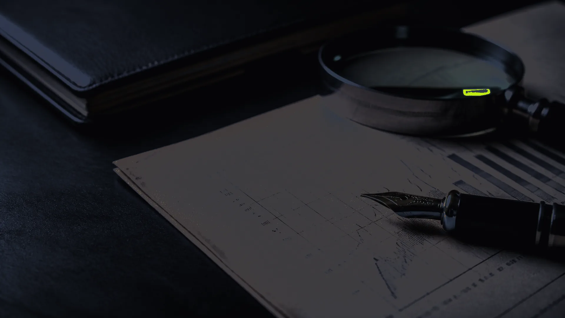 Macro still-life: an illegible printed graph on aged paper beside a fountain pen and a magnifying glass picking up a hint of accent light.